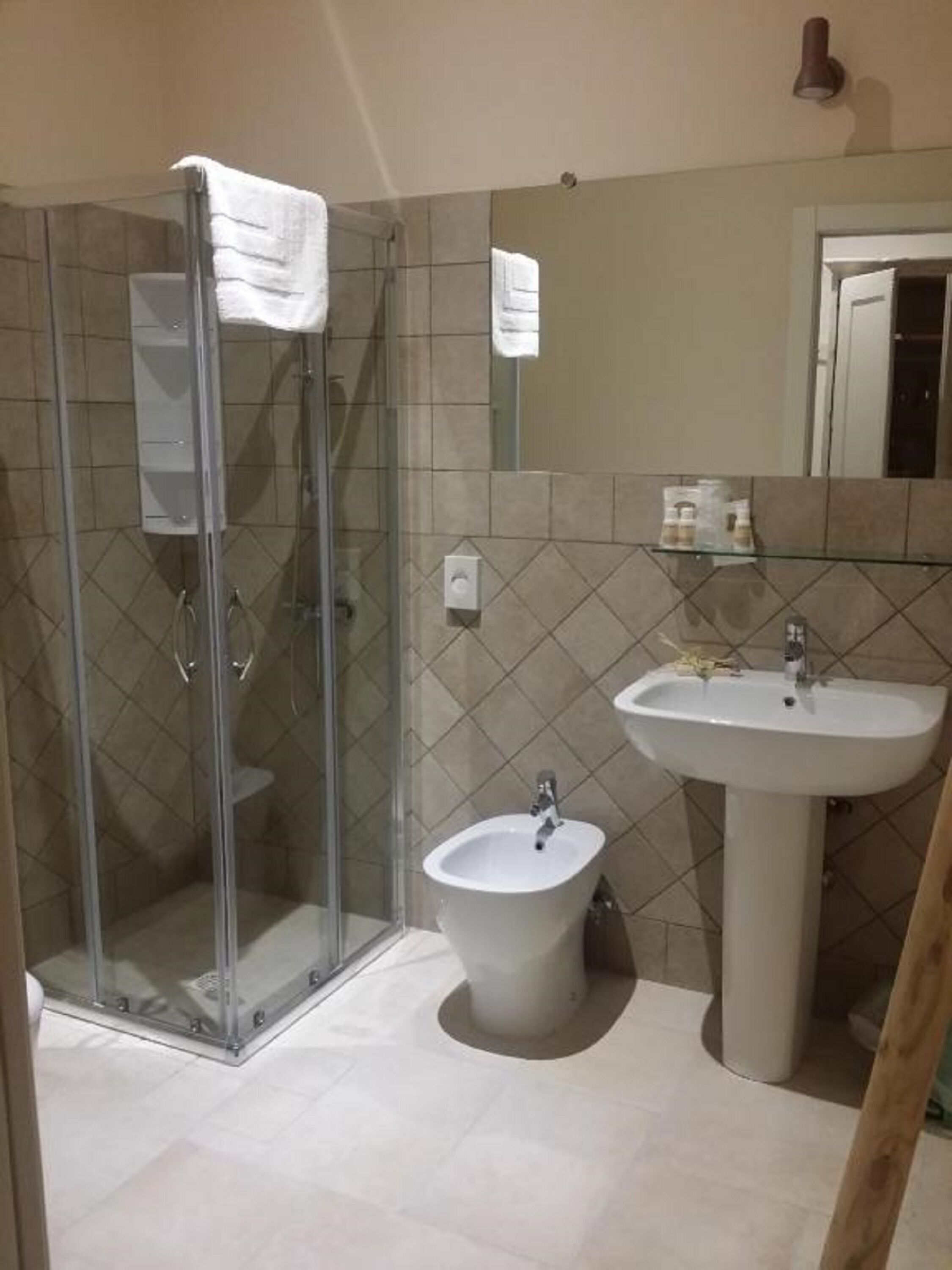 A bathroom with a glass-enclosed shower, a pedestal sink, and a bidet.