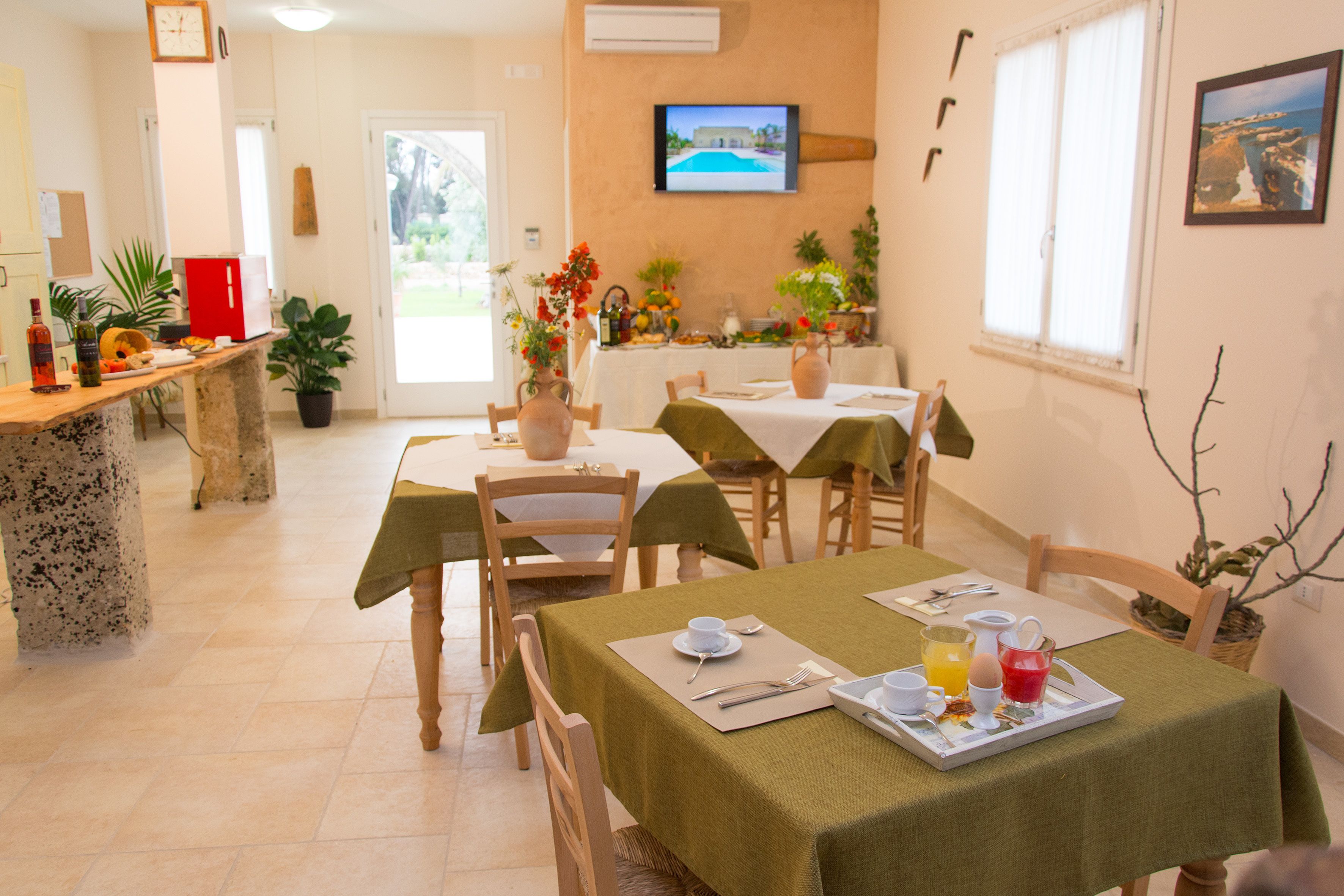 Un coin repas avec des tables préparées pour le petit-déjeuner, un téléviseur fixé au mur et une vue sur l’extérieur.