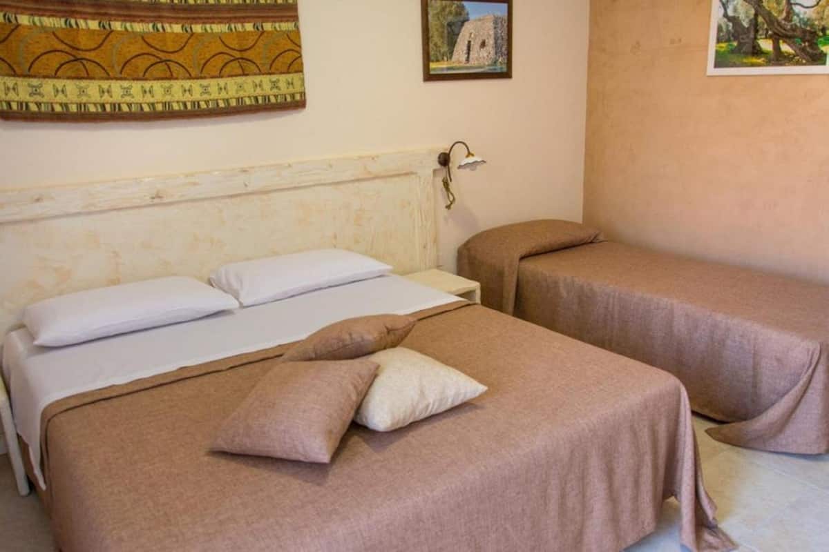 A room with two beds, each with a brown bedspread and pillows. There is a wall-mounted lamp and two framed pictures above the beds.