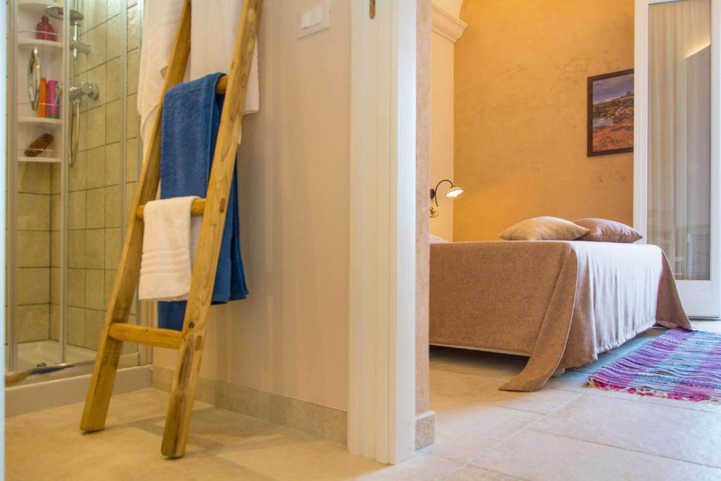 A bathroom with a shower, a wooden ladder, and a bed with a beige bedspread.
