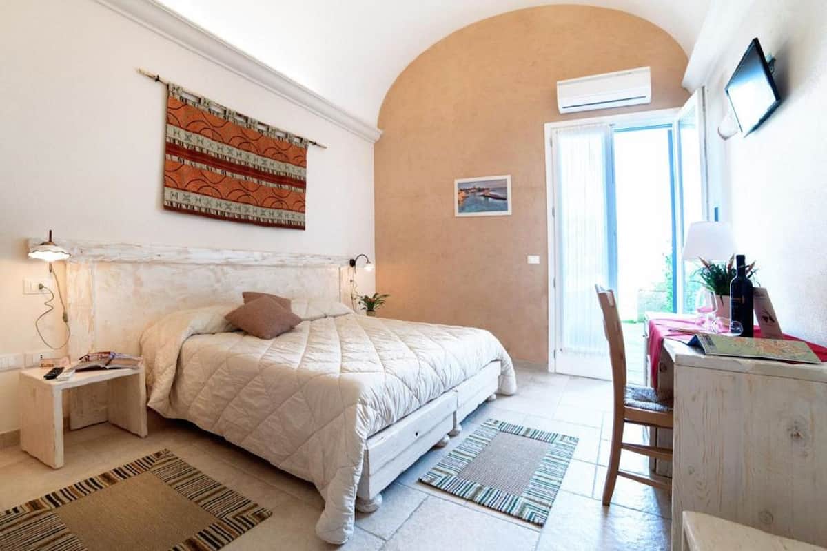 A bedroom with a large bed, bedside tables, a desk, and a chair. There is a window with a view of the outdoors.