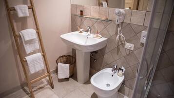 Un baño con un perchero de madera, un lavabo pedestal, un bidé y un estante de vidrio con artículos de aseo.