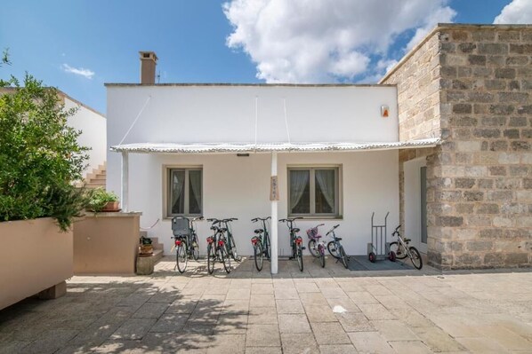 Un edificio con fachada blanca, dos ventanas y un porche donde se ven bicicletas estacionadas.