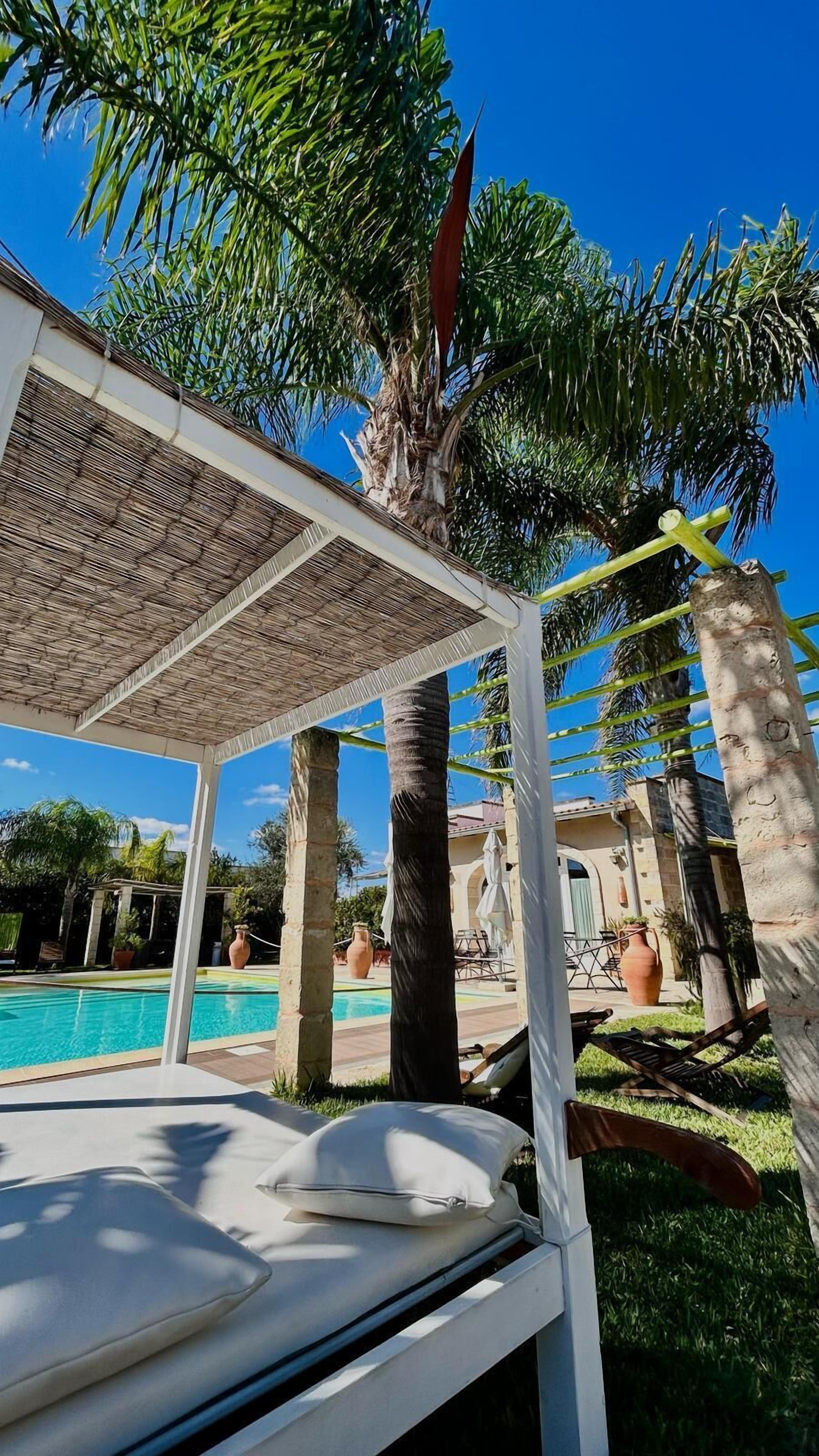 Ein Pool-Loungesbereich mit überdachter Sitzgelegenheit, einem Pool und Palmen.