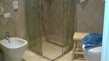 A bathroom with a glass-enclosed shower, a sink, a toilet, and a patterned rug on the floor.