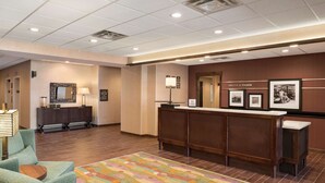 A hotel lobby with a reception desk, a mirror, a sofa, and a colorful rug. - Hampton Inn Lincoln Airport (Lincoln)