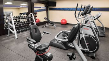 Un gimnasio con equipo de ejercicio variado, incluyendo cintas de correr, una banca y mancuernas.