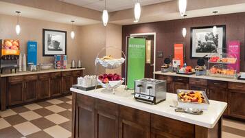 En frukostmatsal på hotellet med ett rutmönstrat golv, träskåp, en fruktskål, en brödrost och olika typer av mat presenterade på ett tilltalande sätt.