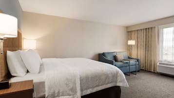 Una habitación de hotel con cama, escritorio, silla y ventana con cortinas.