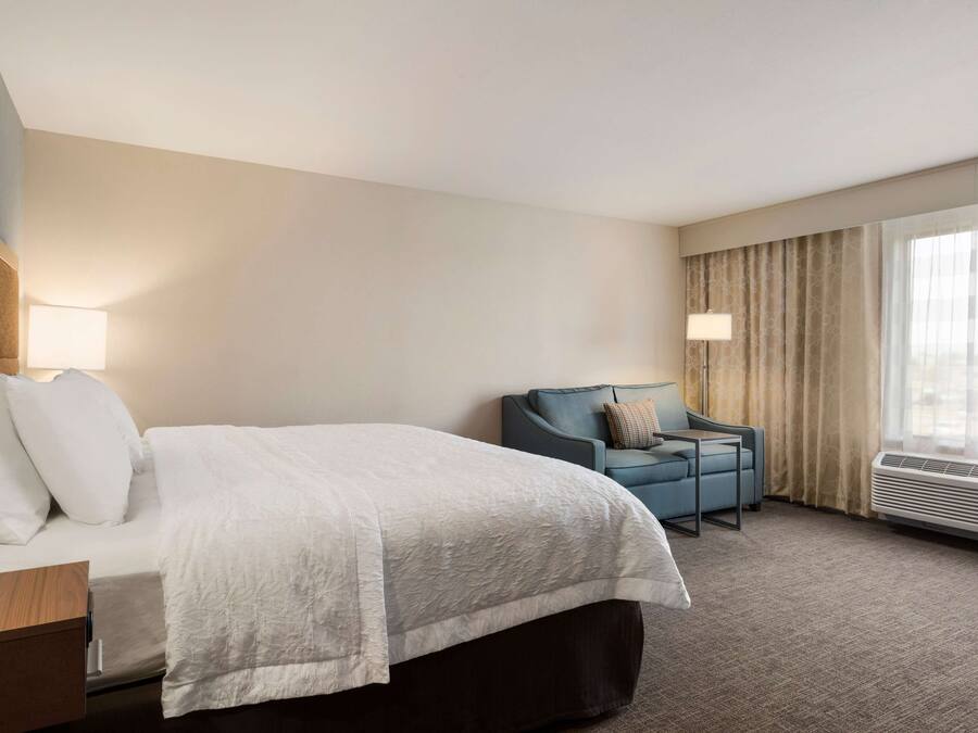 Une chambre d’hôtel avec un lit, un bureau, une chaise et une fenêtre avec des rideaux.
