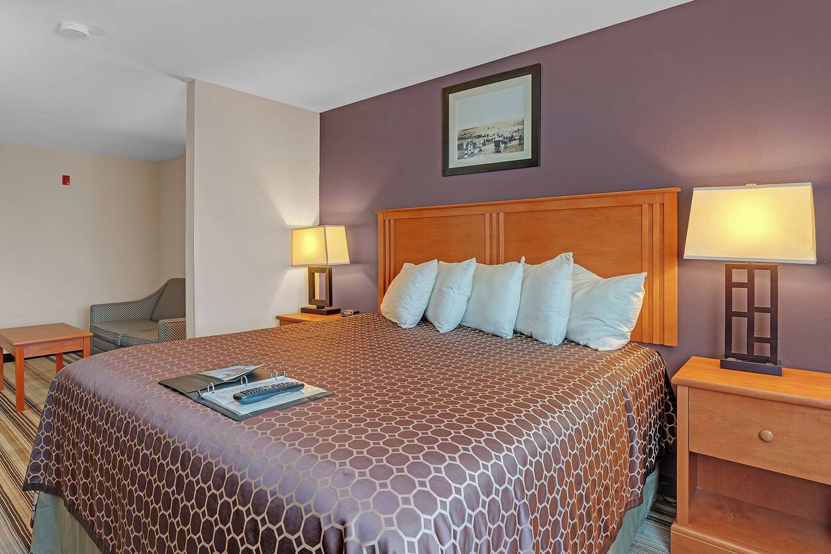 A hotel room with a large bed, two bedside tables, a chair, a framed picture on the wall, and a window.