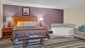 A hotel room with a large bed, a bench, a nightstand with a lamp, a framed picture on the wall, a bathtub, and a sofa. - Bowman Lodge & Convention Center (Bowman)