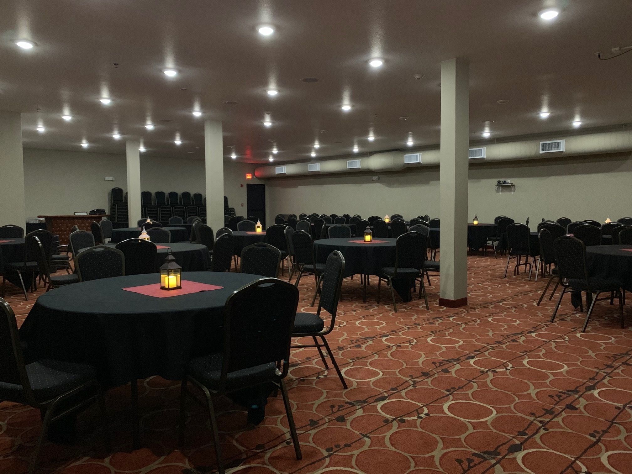 Un salón de conferencias con varias mesas redondas, sillas negras e iluminación colgante.