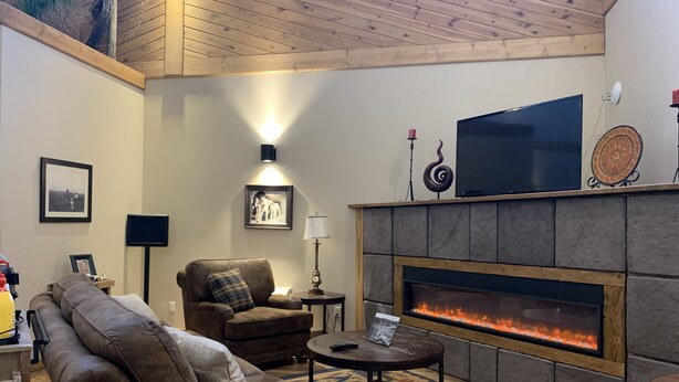 A cozy living room with a fireplace, leather sofas, a television, and a patterned rug. - Bowman Lodge & Convention Center (Bowman)