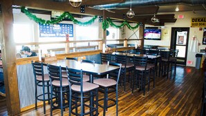 A restaurant interior with wooden flooring, multiple tables and chairs, and a counter area with a menu board. - Bowman Lodge & Convention Center (Bowman)