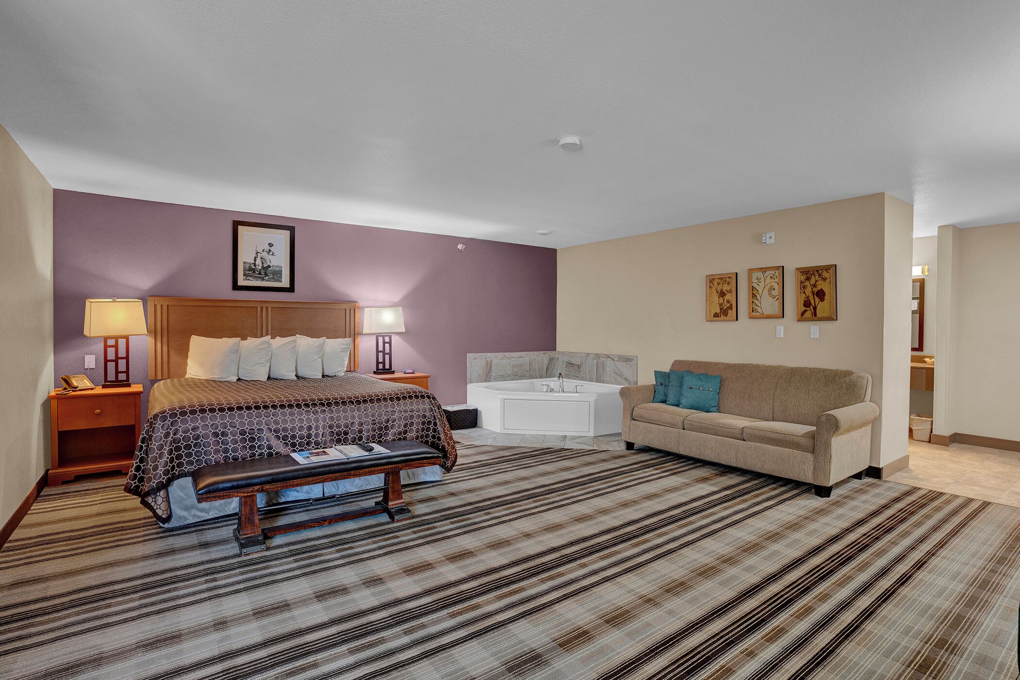 A hotel room with a bed, a bench, a sofa, a bathtub, and a wall with three framed pictures.