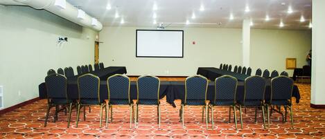 Una sala de conferencias con una pantalla grande, filas de sillas y una alfombra estampada.