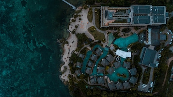 Vista aérea de un resort con varias piscinas, un edificio grande de techo plano y una zona de playa.