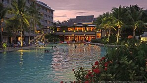 A hotel with a swimming pool, palm trees, and a building with multiple floors and balconies. - BE Grand Resort Bohol (Panglao)