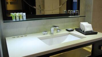 A hotel bathroom with a white sink, a mirror, and a glass shelf above the sink.
