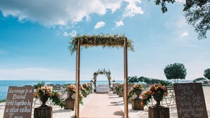 A beach wedding setup with a wooden archway, floral decorations, and a sandy aisle. - BE Grand Resort Bohol (Panglao)