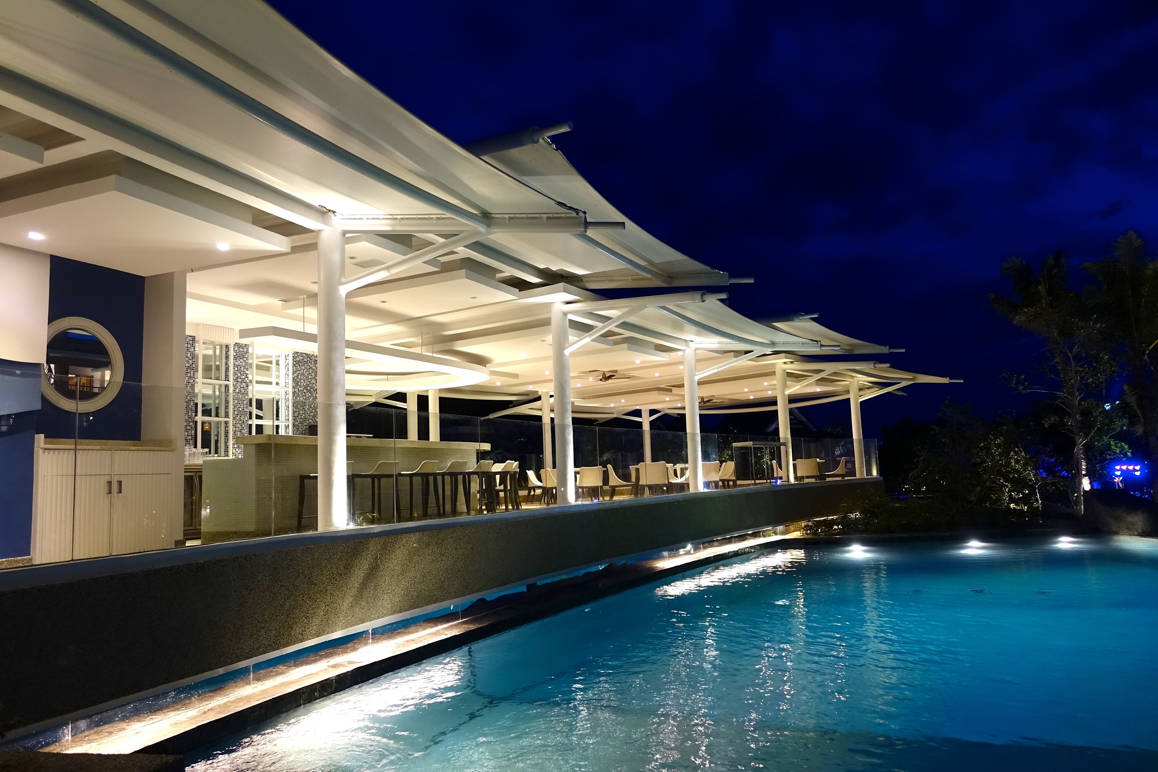 A poolside area with a covered seating area, a pool, and a bar.