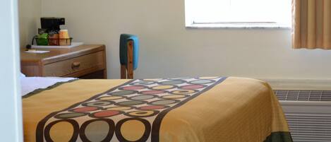 A hotel room with a bed, a nightstand, a lamp, a window with curtains, and a heater.