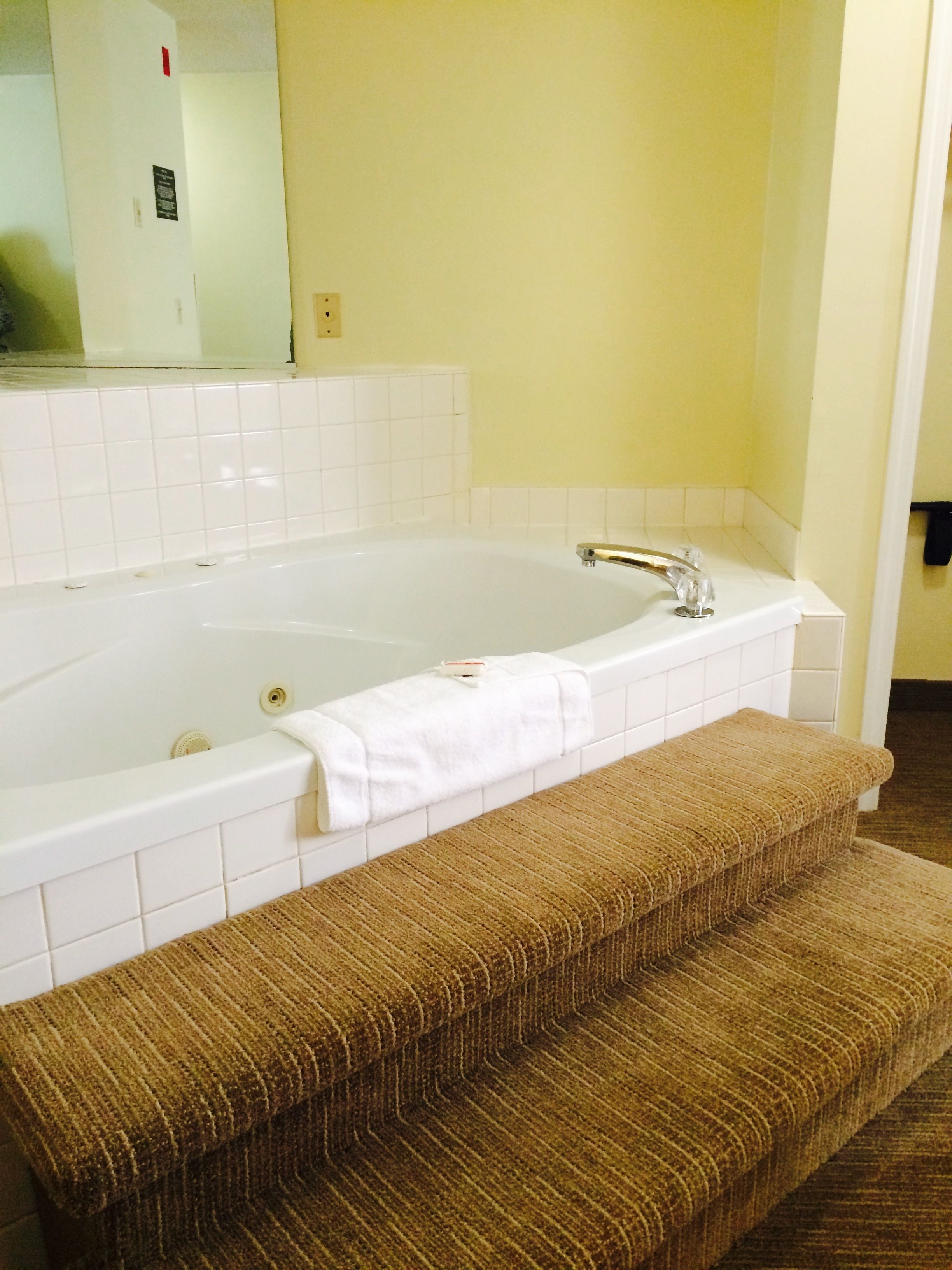 Ein Badezimmer mit einer großen weißen Badewanne, einer Holzbank und einem Spiegel an der Wand.