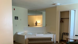 Ett hotellrum med ett stort badkar, en spegel, ett litet bord med stolar och en klädställning.