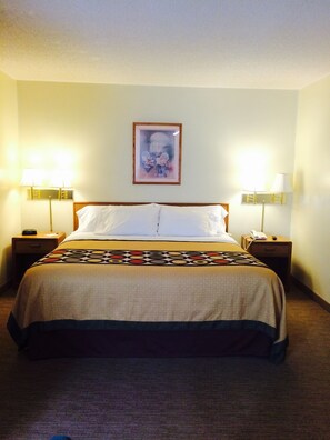 A hotel room with a bed, two bedside tables with lamps, a framed picture on the wall, and a carpeted floor. - Brookshire Inn (Inez)
