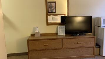Una habitación de hotel con un aparador de madera, un televisor de pantalla plana, un microondas y una cama con una colcha estampada.