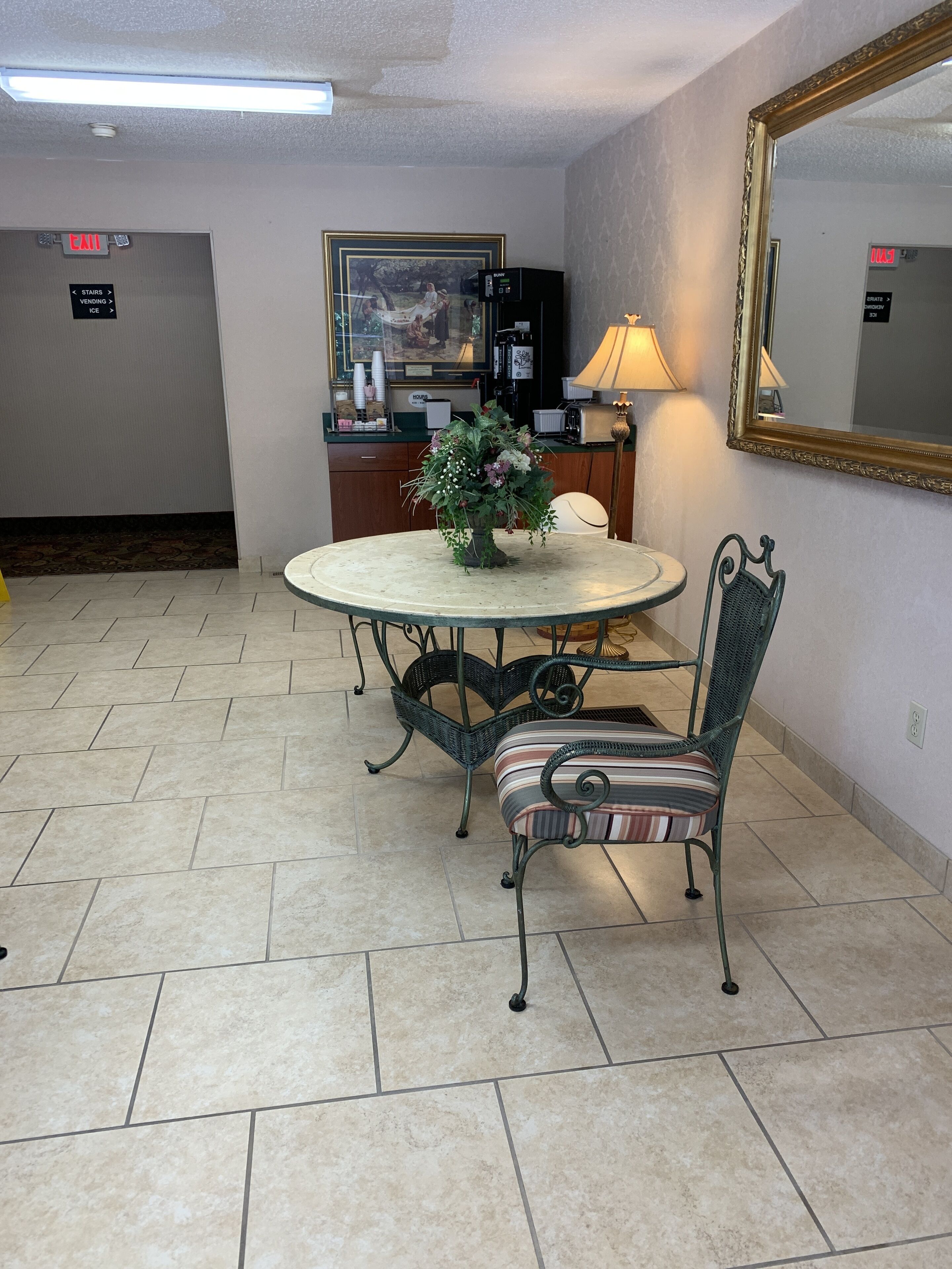 Un coin repas avec une table ronde, des chaises, un arrangement floral en guise de centre de table, une machine à café et un miroir au mur.
