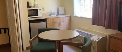 Cocina compacta con microondas, lavamanos y refrigerador. Zona de comedor con mesa y sillas.