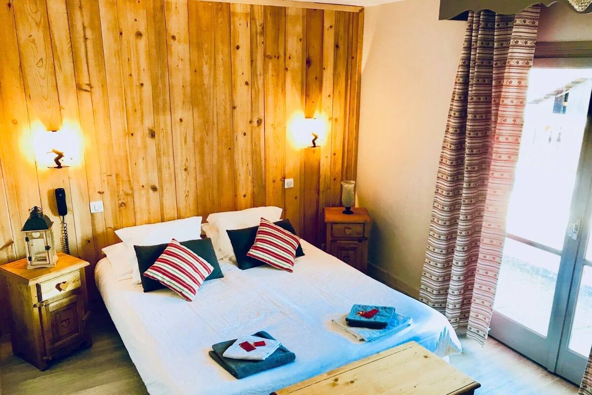 Ein Zimmer mit Holzwänden, einem Bett, zwei Nachttischen und einem Fenster mit Vorhängen.