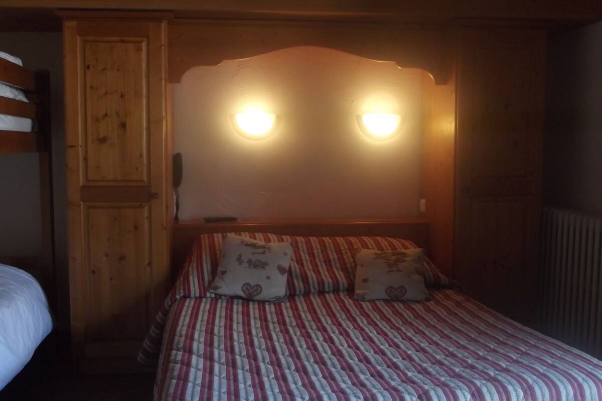 Ein Schlafzimmer mit einem Etagenbett links und einem Einzelbett mit gestreifter Bettwäsche und Kissen mit Herzmuster. Über dem Einzelbett befinden sich zwei Wandleuchten.