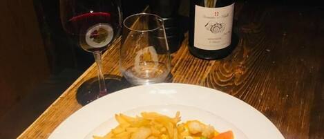 Un plato de comida con carne, papas fritas y vegetales, una botella de vino y dos copas sobre una mesa de madera.
