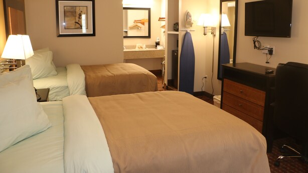 Habitación de hotel con dos camas, un escritorio, una silla, un televisor y un baño visible a través de una puerta abierta.