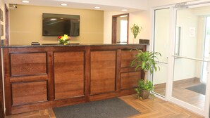 Un área de recepción con un mostrador de madera, un televisor de pantalla plana en la pared, una planta en maceta y una señal de salida.