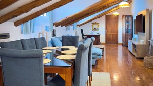 A dining area with a wooden table and chairs, a high ceiling with exposed beams, and a view of the living room in the background. - Illa Hotel (Cusco)