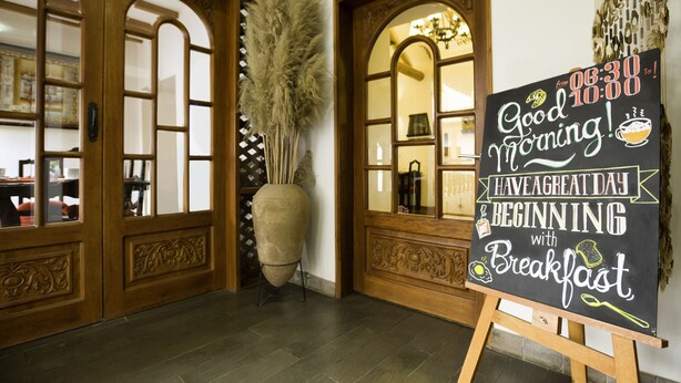 A room with wooden doors, a large vase with pampas grass, and a chalkboard sign with a breakfast message. - Illa Hotel (Cusco)