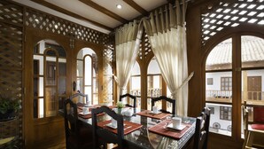 A dining area with a glass table, wooden chairs, and a view through large windows. - Illa Hotel (Cusco)