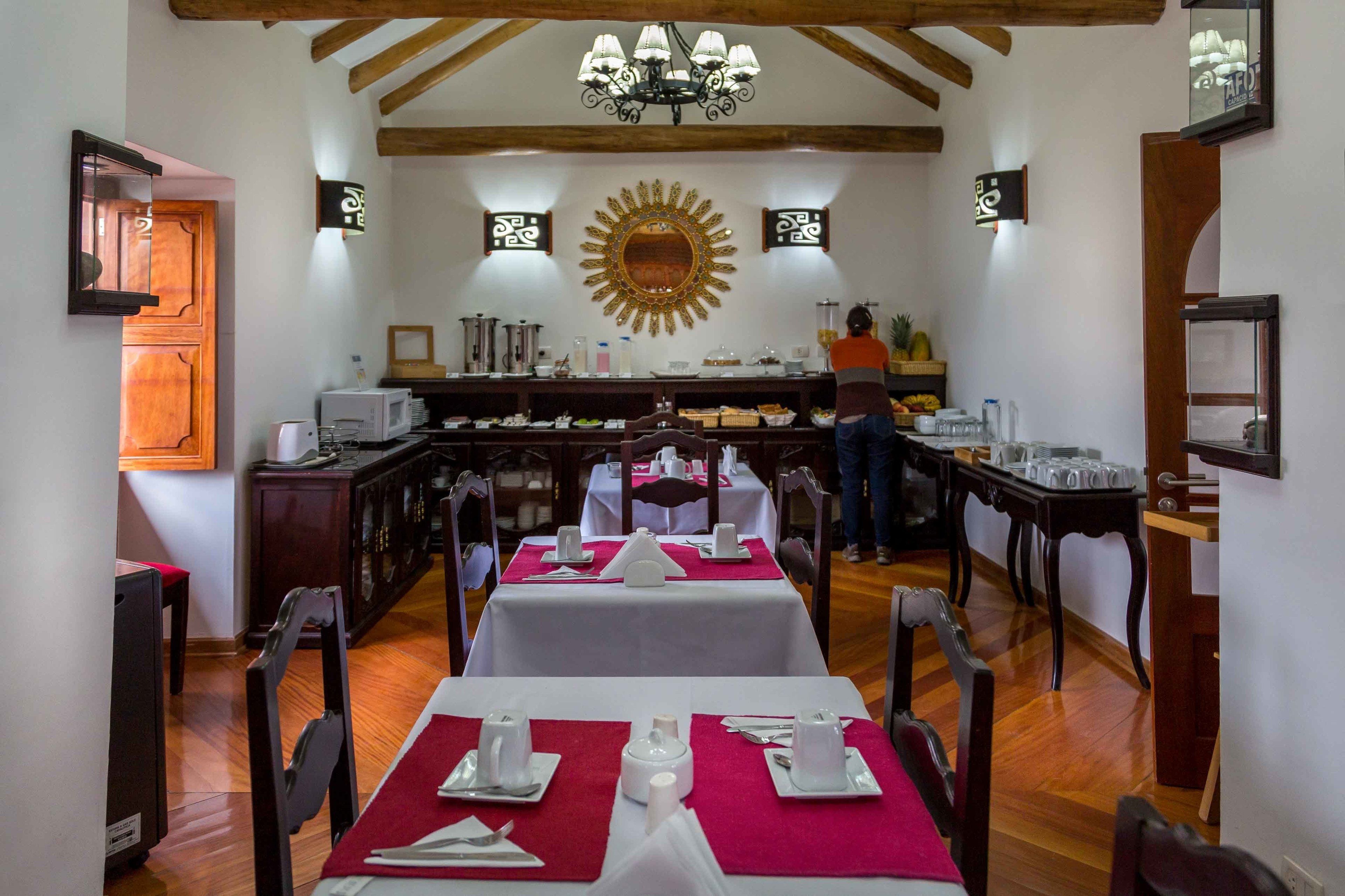 Un coin repas avec des tables dressées pour le repas, une cuisine en arrière-plan et un soleil décoratif peint sur le mur.