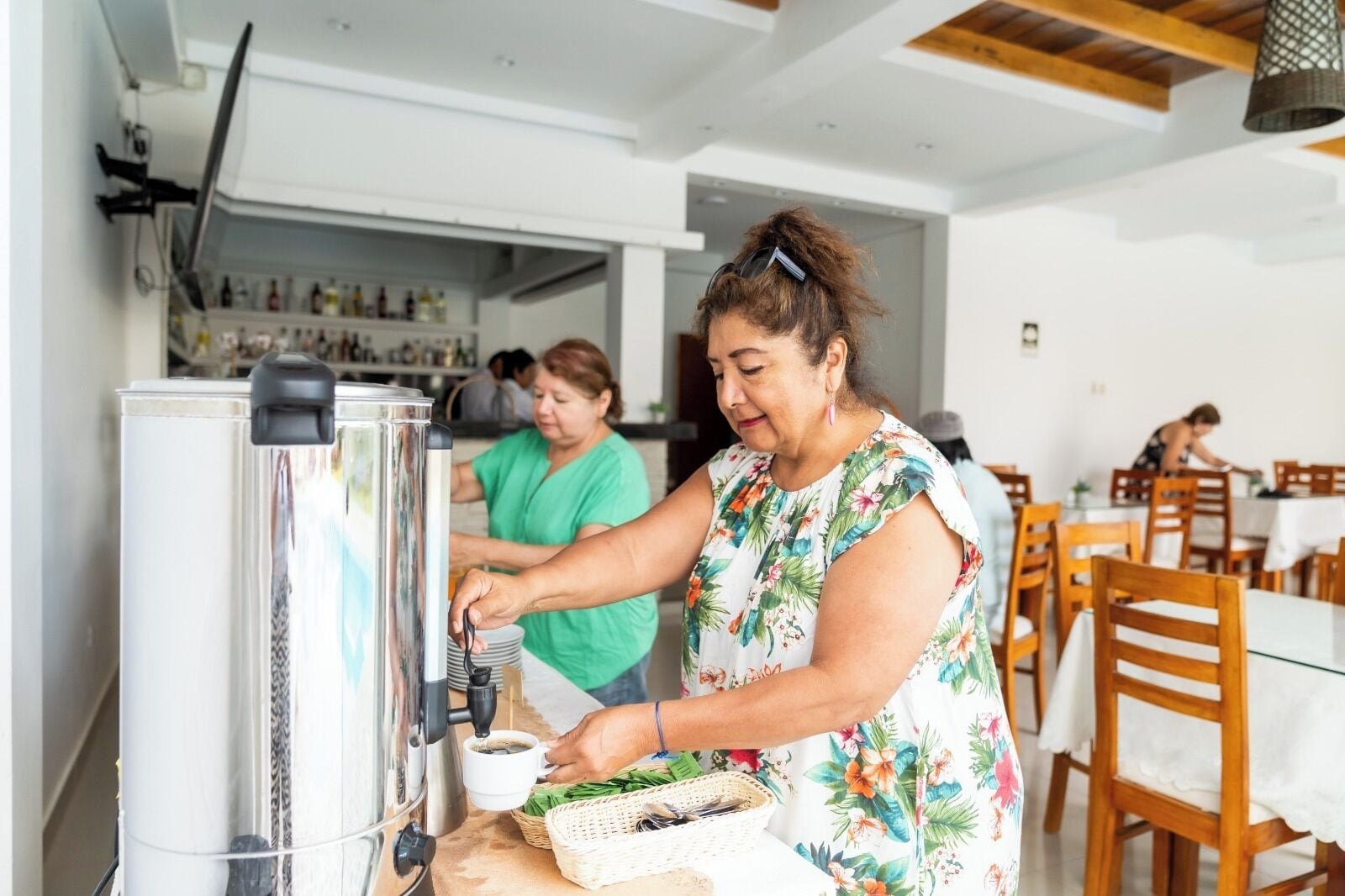 Una persona preparando café en una cafetera en una cocina moderna con muebles de madera y una barra visible al fondo.