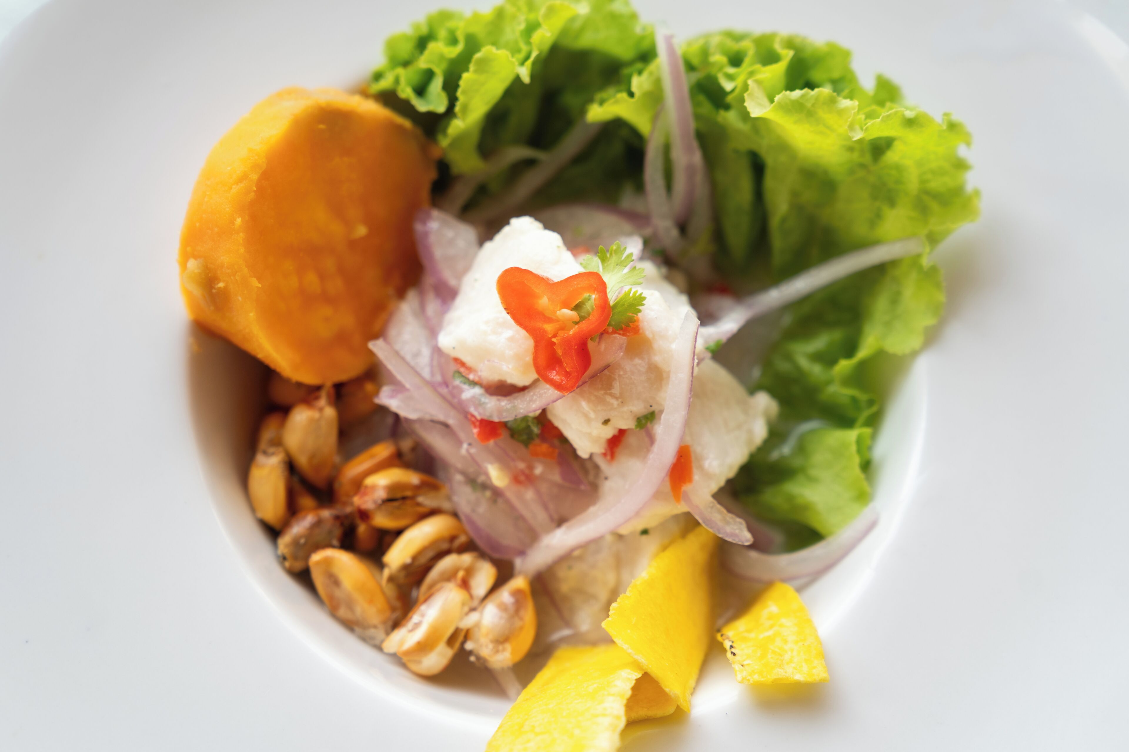 A dish with various ingredients including a yellow fruit, red onion, and green leaves.