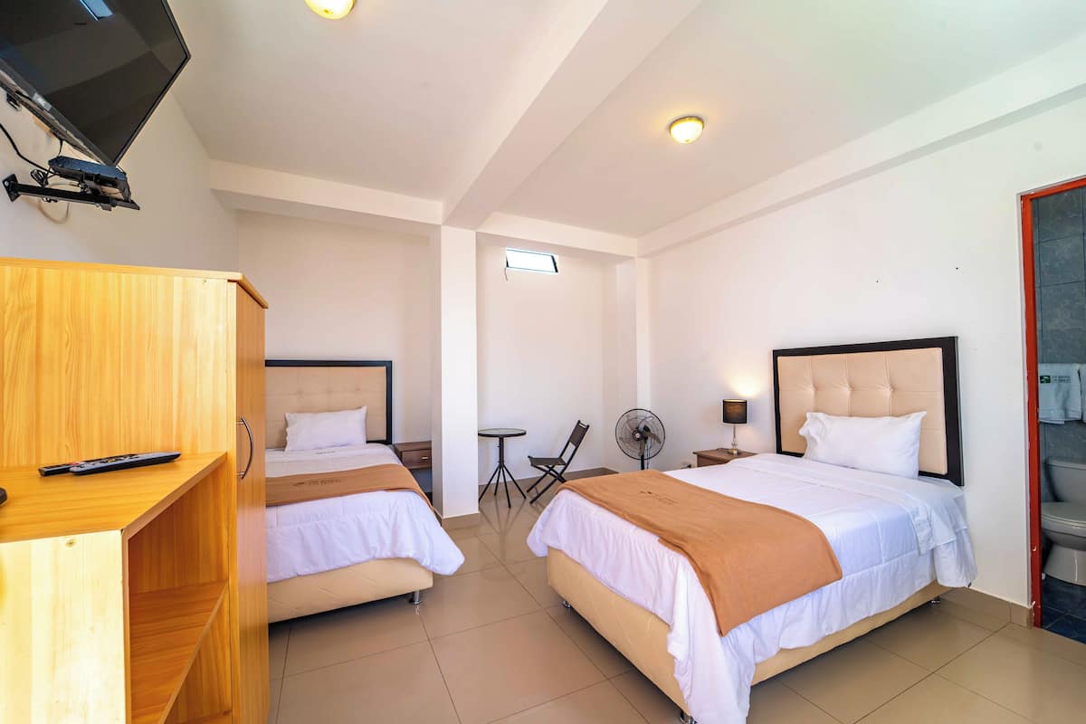 A hotel room with two beds, a TV, a desk, and a small table with a chair.