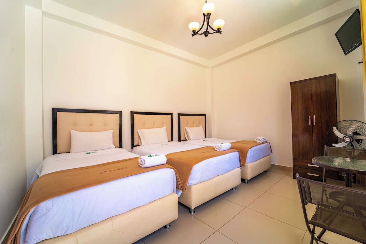 A hotel room with three beds, a dining table, and a fan.