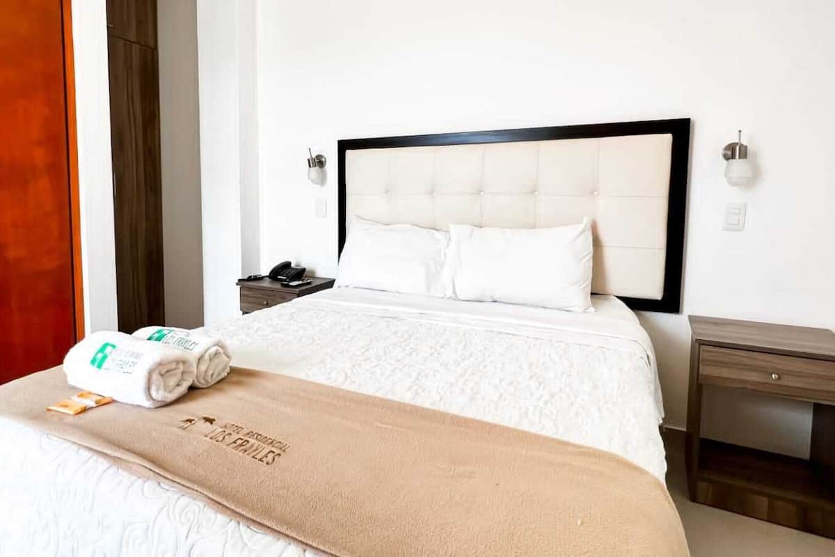 A hotel room with a bed, a nightstand, a wooden door, and a wall-mounted light fixture.