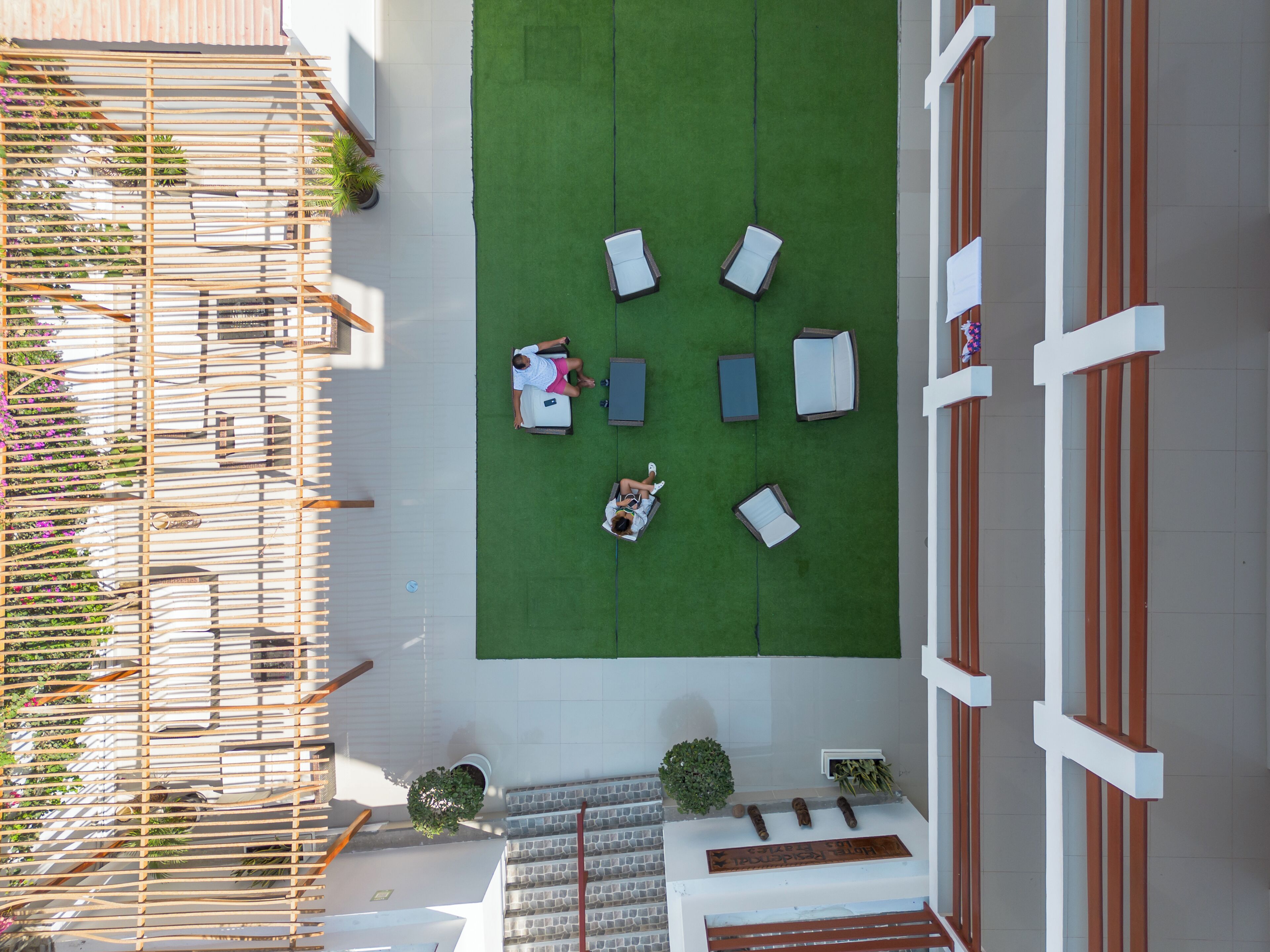 Vista aérea de un jardín en la azotea con una zona de estar, una pérgola de madera y una escalera que conduce a un nivel superior.