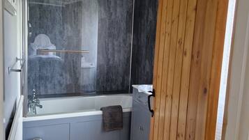 A modern bathroom with a bathtub, grey cabinets, and a wooden floor.