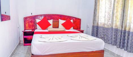Una camera d'albergo con un letto in legno, cuscini rossi e bianchi, una coperta bianca e un tappeto a righe verdi e gialle.